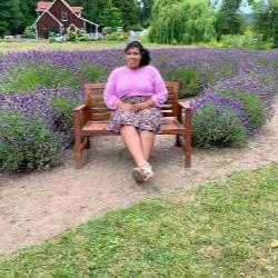 An artist sits at a park bench wearing a pink sweater